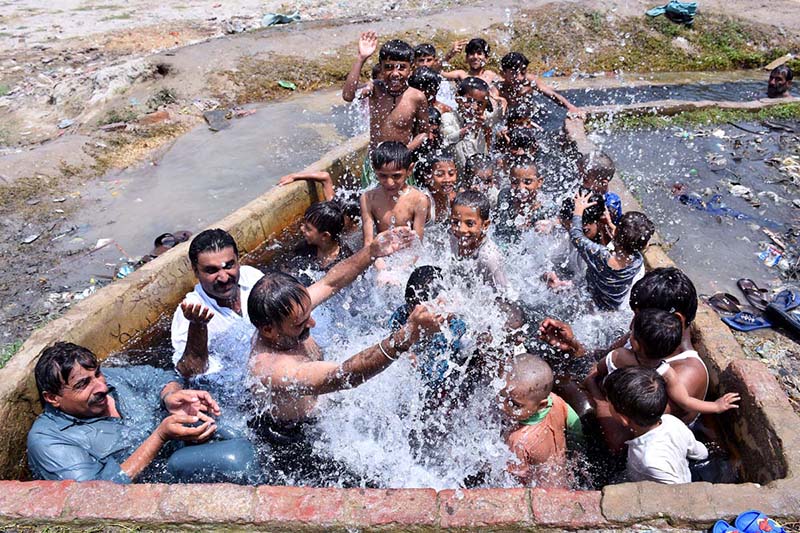 People along with children enjoying bathing in the watercourse to get some relief from hot weather in Ghulam Bhutto Village