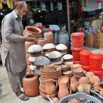 A shopkeeper arranging and displaying clay-made cooking pots to attract the customers at Terlai Road