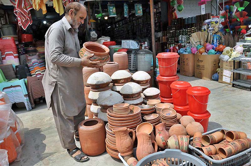 A shopkeeper arranging and displaying clay-made cooking pots to attract the customers at Terlai Road