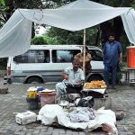 A vendor busy in frying samosa for customers at bus stop