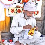 A skilled person making embroidery work on pillow to attract the customer at his road side setup
