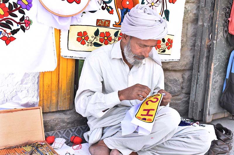 A skilled person making embroidery work on pillow to attract the customer at his road side setup