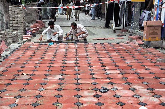 Labourers busy in fixing tiles on footpath at Aabpara Market.