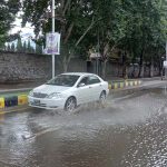 Vehicle passing through stagnant rain water accumulated on road during heavy rain in city