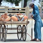 A vendor is pumping air into the tire of hand cart by using hand pump at Latifabad