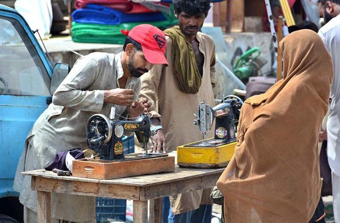 Mechanic busy in repairing sewing machine of woman customer at his roadside setup