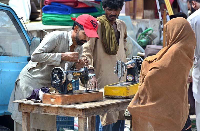 Mechanic busy in repairing sewing machine of woman customer at his roadside setup
