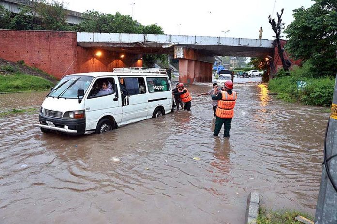 Rescue worker pushing an out of order vehicle which stuck in water accumulated on road due to torrential rain since last night
