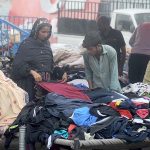 People selecting and purchasing old clothes displayed by the roadside vendor to attract the customers.