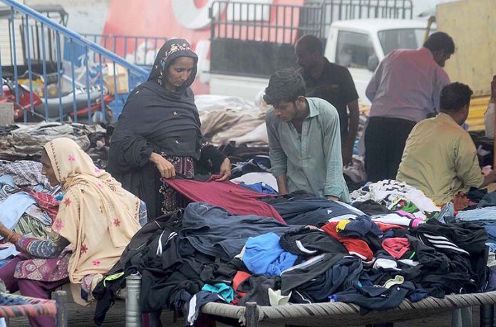People selecting and purchasing old clothes displayed by the roadside vendor to attract the customers.