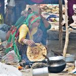 A gypsy woman preparing bread (Roti) for children in her makeshift house at Latifabad