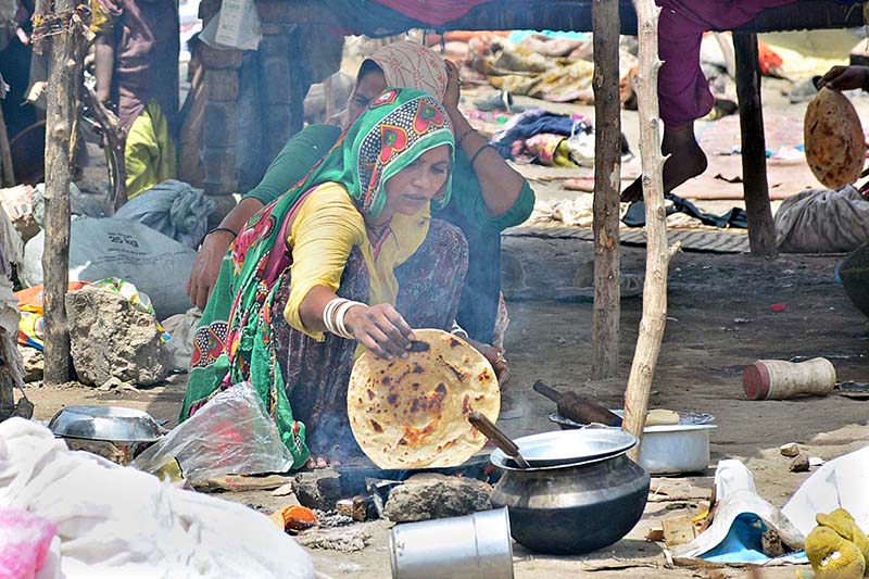 A gypsy woman preparing bread (Roti) for children in her makeshift house at Latifabad