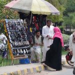 A lady selecting and purchasing sunglasses from a roadside vendor