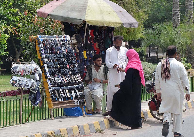 A lady selecting and purchasing sunglasses from a roadside vendor