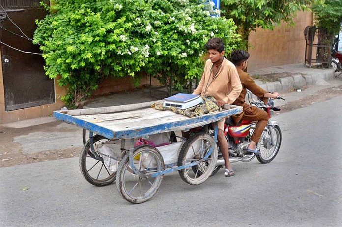 A person holding hand cart while sitting on rear seat of a motorcycle at General Bus Stand Road