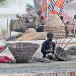 A gypsy family preparing traditional baskets with dry tree branches while sitting at the banks of a canal