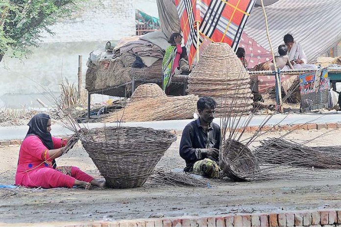 A gypsy family preparing traditional baskets with dry tree branches while sitting at the banks of a canal
