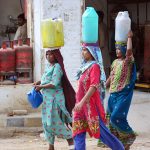Gypsy women carrying pots on her head back after filling clean water at Qasimabad