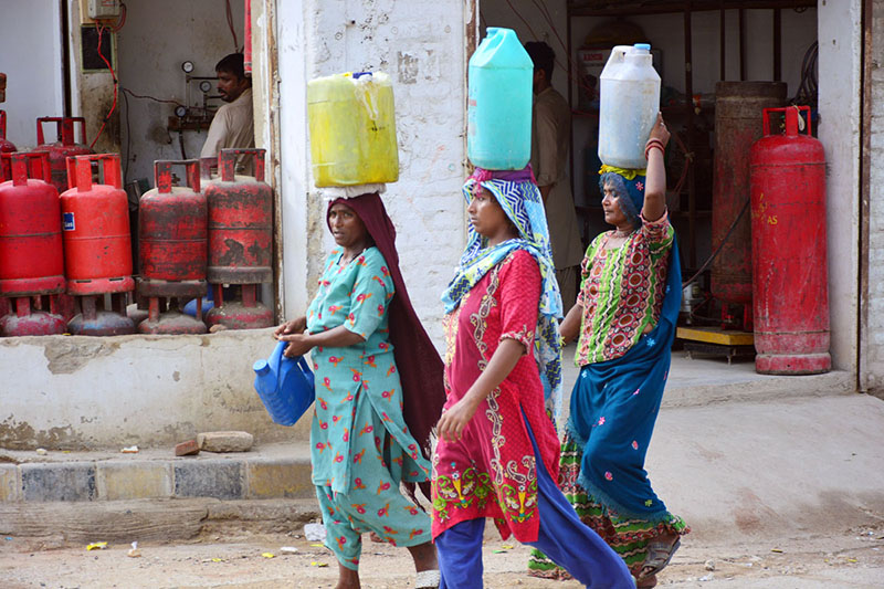 Gypsy women carrying pots on her head back after filling clean water at Qasimabad