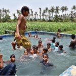 Youngsters bathing in a pond of tube well to get relief from scorching hot weather in the city