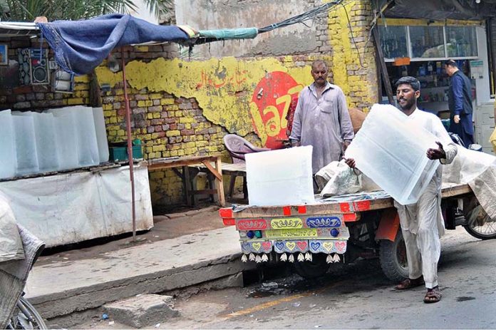A labourer busy in unloading ice blocks from a delivery van at his roadside setup as demand increased during hot weather