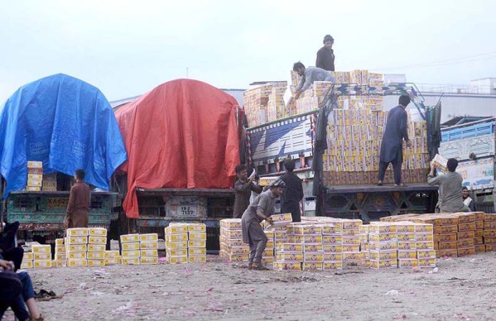 Laborers busy unloading of peach boxes from delivery truck at Pirwadhai Fruit Market.