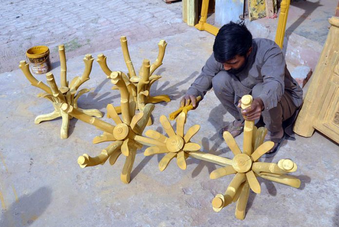 A wood worker given the final touches and polishes on a clothes hanger stand at Shahdara Furniture Market