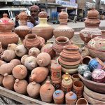A vendor arranging and displaying clay made pots at his roadside setup near New Bus Stand
