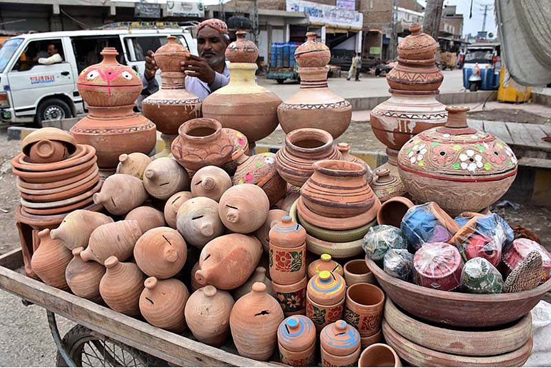 A vendor arranging and displaying clay made pots at his roadside setup near New Bus Stand