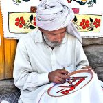 A skilled person making embroidery work on bed sheet and pillow to attract customer at his road side setup