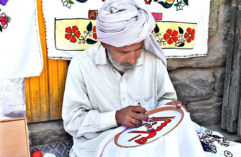 A skilled person making embroidery work on bed sheet and pillow to attract customer at his road side setup