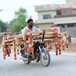 A motorcyclist on the way loaded with frames of a traditional bed (charpai) heading towards his destination