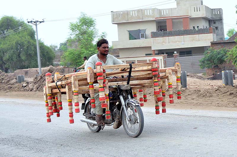 A motorcyclist on the way loaded with frames of a traditional bed (charpai) heading towards his destination