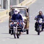 Motorcyclist on the way cover his face with piece of cloth to protect from direct sunlight during hot weather in the city