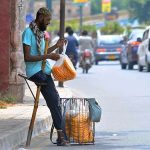 A disabled person selling edible stuff at a roadside during hot and humid weather