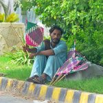 A street vendor selling traditional handmade fans while sitting roadside footpath during hot and humid weather