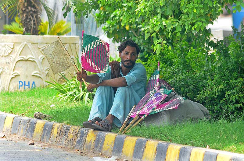 A street vendor selling traditional handmade fans while sitting roadside footpath during hot and humid weather