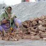 Lady labourer busy in crushing bricks into pieces for construction use