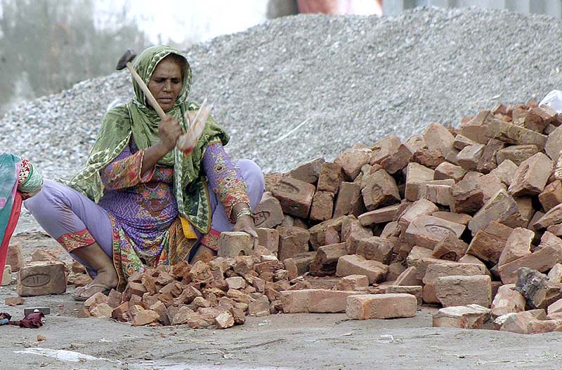 Lady labourer busy in crushing bricks into pieces for construction use