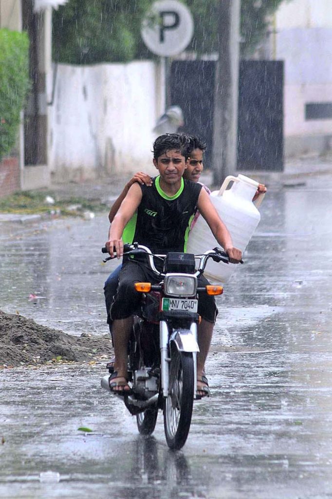 A motorcyclist on the way under cover of a piece of cloth to protect from monsoon rain in the city