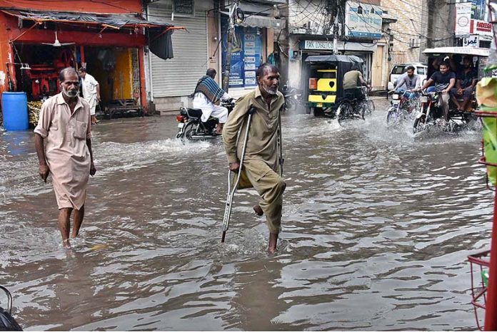 A disable old person passing through rain water accumulated on road after heavy rain that experienced the city