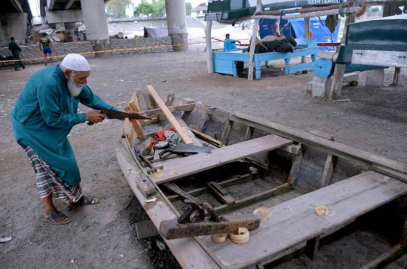 An elderly man is preparing a wooden boat near the Ravi River