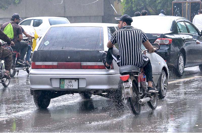 A motorcyclist is pushing a damaged vehicle with the help of his feet during the monsoon rains in the provincial capital