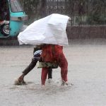 Woman with her son under the cover of a piece of plastic bag to protect herself from monsoon rain in the city