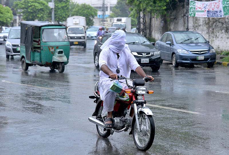 A motorcyclist is pushing a damaged vehicle with the help of his feet during the monsoon rains in the provincial capital