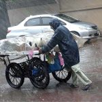 An aged person pushing his handcart loading with vegetable during heavy rain in the city