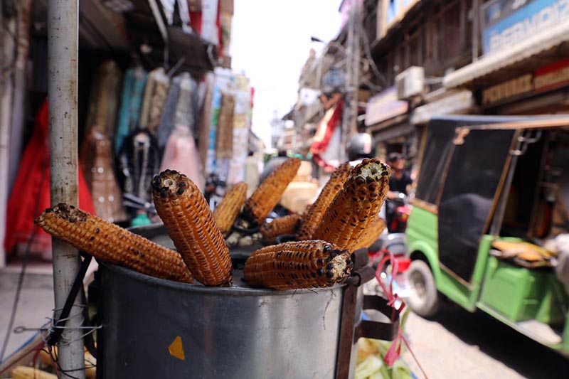 A vendor selling roasted corn cobs to attract customers at his roadside setup in the city