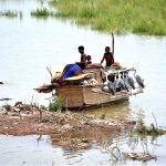 Youngsters sitting on a boat loaded with luggage parked at right bank of Indus River after flood warning