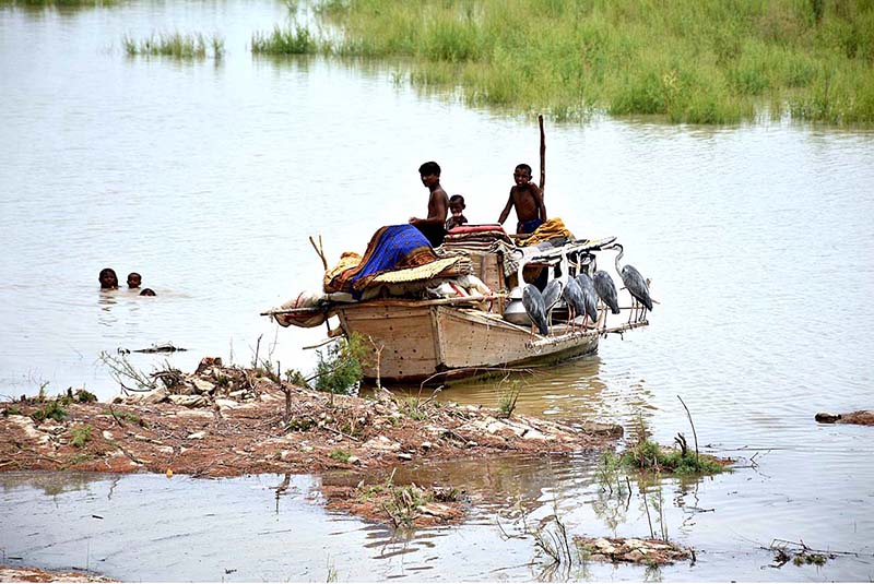Youngsters sitting on a boat loaded with luggage parked at right bank of Indus River after flood warning