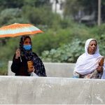 A woman on the way under cover of an umbrella to protect from direct sunlight during hot and humid weather at Pirwadai